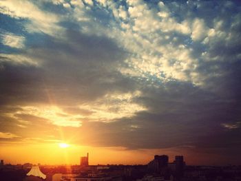 Silhouette of cityscape against cloudy sky at sunset