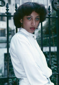 Close-up portrait of young woman standing by fence