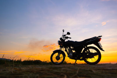 Silhouette person riding bicycle on field against sky during sunset