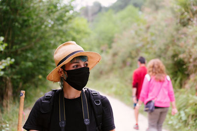 Traveling woman wearing protective mask walking along road in woods and looking away during summer holiday