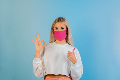 Portrait of beautiful young woman wearing mask gesturing against blue background