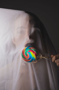 Portrait of woman under textile licking lollipop