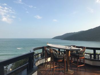 Chairs and table by sea against sky