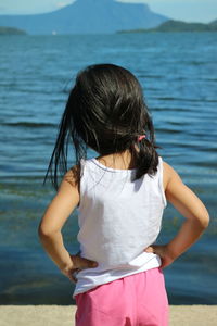 Rear view of girl with hands on hip looking at lake