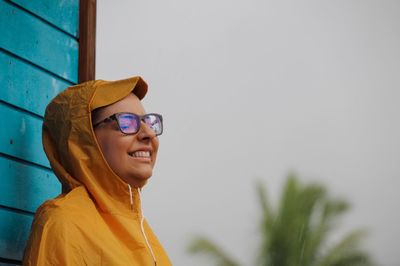 Side view of smiling young woman wearing sunglasses and raincoat during rainy season