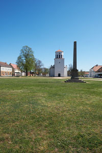 Houses and trees on field against clear blue sky