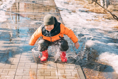 Gleeful puddles, child red boots send cascade of droplets, celebration of melting snow on sunny day