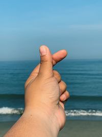 Cropped hand of person gesturing against sea and sky