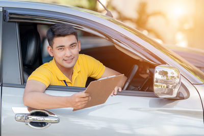 Portrait of smiling young man with clipboard sitting in car 