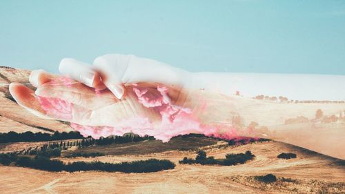 Collage of hand with pink clouds over tuscany land
