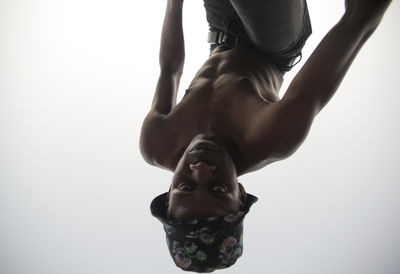 Low angle view of young woman exercising against clear sky