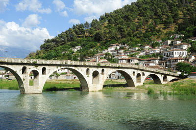 Arch bridge over river in city against sky