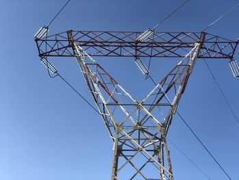 Low angle view of electricity pylon against clear blue sky