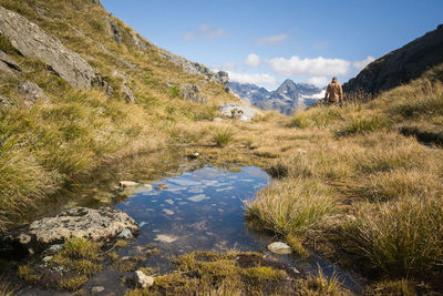 Rear view of man standing on grassy field amidst mountain against sky