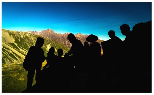 Silhouette people on rock against sky