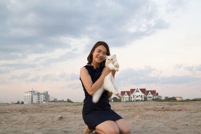 Full length of woman holding cat on sand against sky