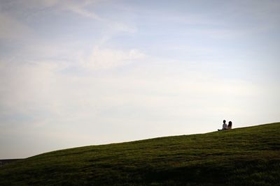 Low angle view of people sitting on grassy hill against sky