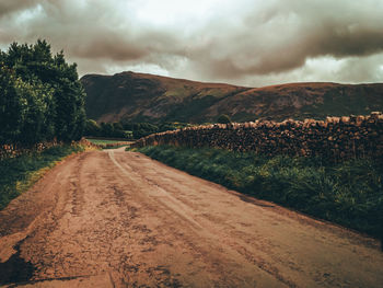 Dirt road along landscape and mountains against sky