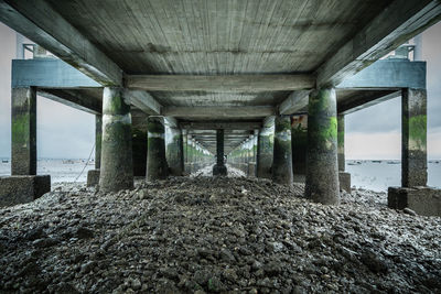 Columns of pier at beach against sky