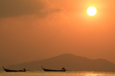 Silhouette people on sea against orange sky