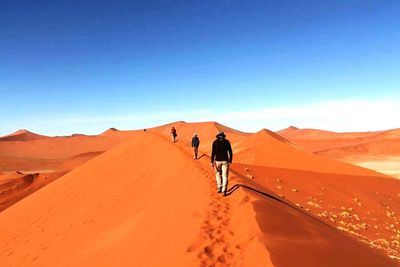 Rear view of man walking on desert against clear blue sky