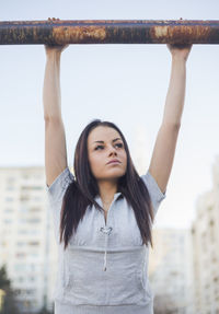 Woman hanging on rusty pole against sky