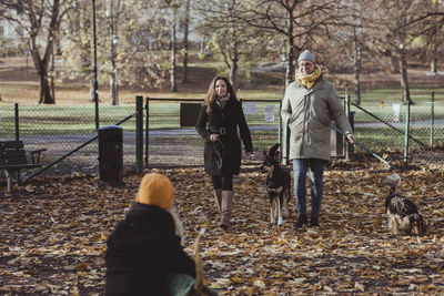 Full length smiling male and female pet owners walking with dogs at park