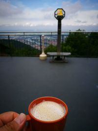 Close-up of hand holding drink by river against sky