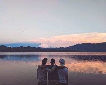 Rear view of friends on water against sky during sunset