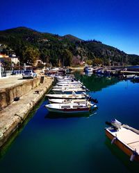 Boats moored at harbor against clear blue sky