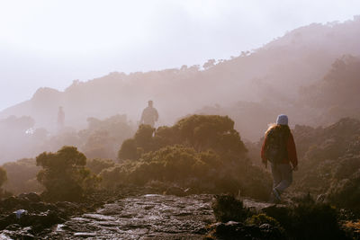 Rear view of people walking on mountain against sky