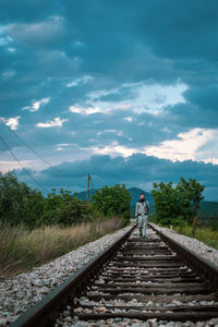 Rear view of man standing on railroad track against sky