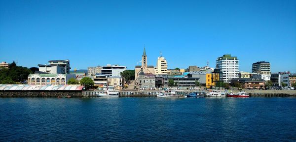 River by cityscape against clear blue sky