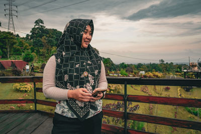 Portrait of young woman standing against fence