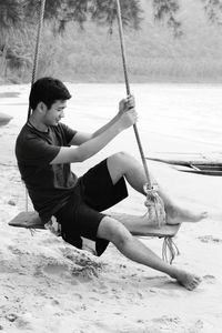 Man sitting on rope swing at beach