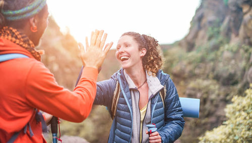 Smiling woman giving high-five to friend while standing against mountains