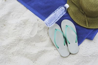 High angle view of flip-flops and bottle at sandy beach