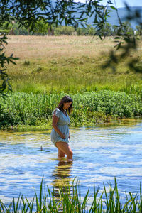 Girl wearing sundress, walking knee deep in creek on a hot day in summer