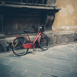 Red bicycle parked by wall on sidewalk