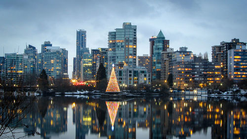 Illuminated buildings by river against sky at dusk