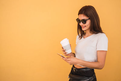 Young woman wearing sunglasses standing against yellow background