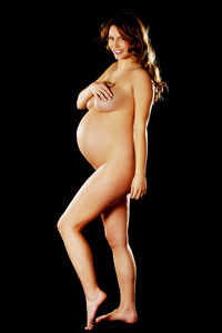 Portrait of naked pregnant woman smiling while standing over black background