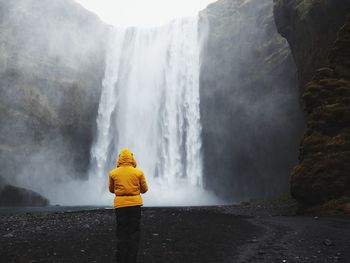 Rear view of woman standing against waterfall