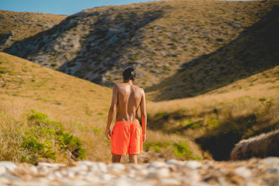 Rear view of shirtless man walking on dirt road