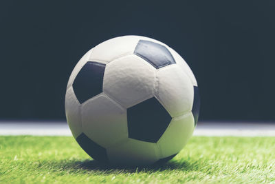 Close-up of soccer ball on grassy field against black background