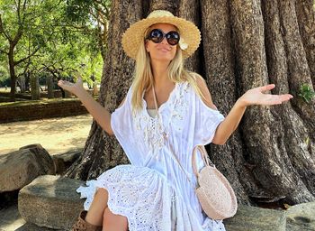 Portrait of woman wearing sunglasses sitting against tree trunk