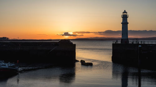 Silhouette lighthouse by sea against sky during sunset