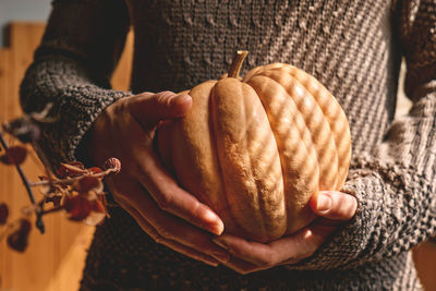 Female in knitted brown woolen sweater holding orange pumpkin. cozy autumn vibes. fall mood.