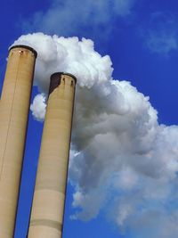 Low angle view of smoke emitting from chimney against blue sky