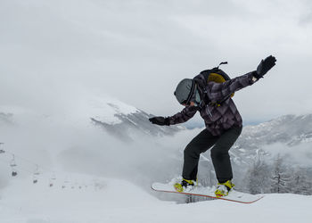 Man snowboarding over land against cloudy sky